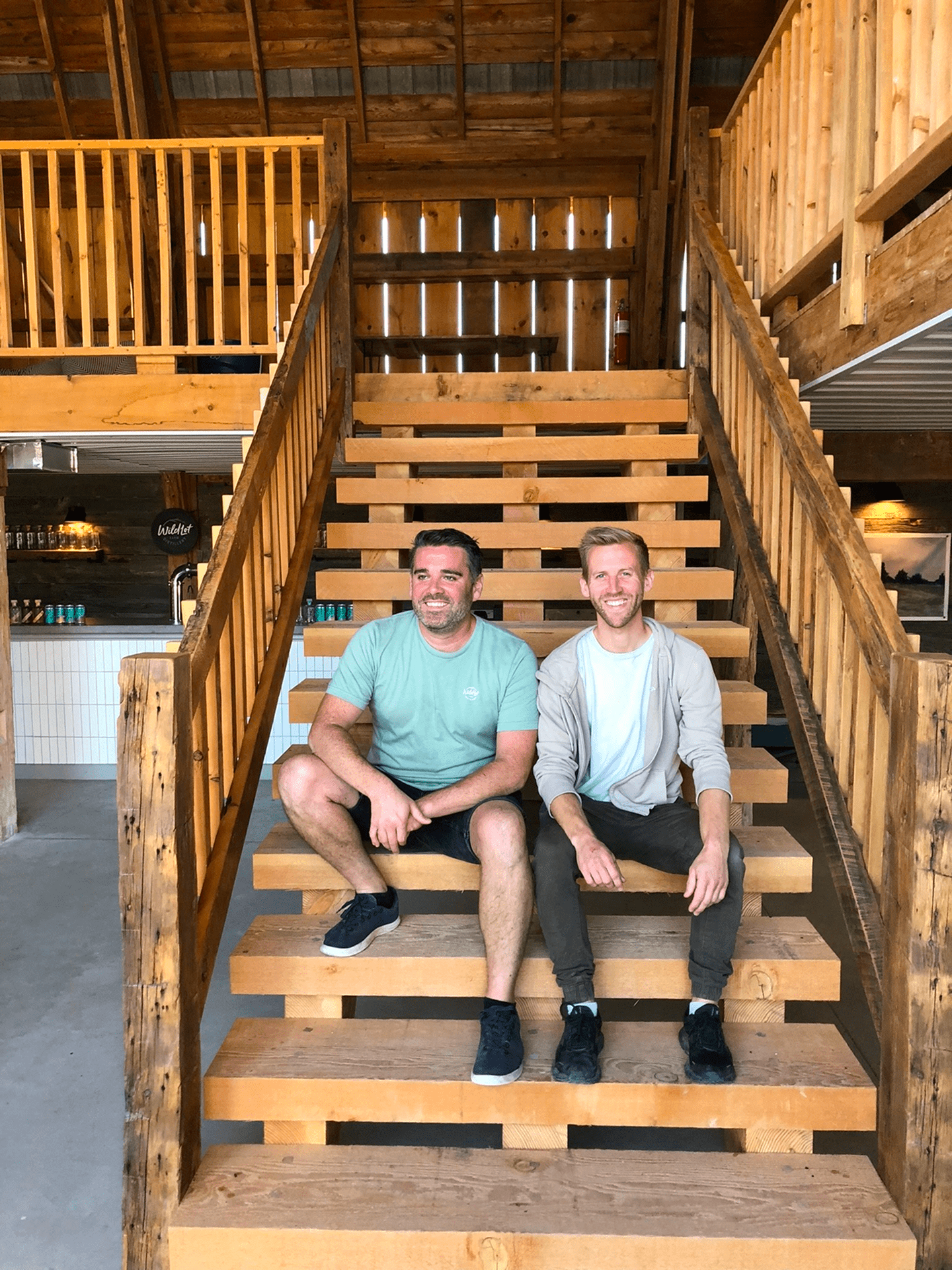 Ryan & Taylor sitting on a wooden staircase inside a wooden barn.