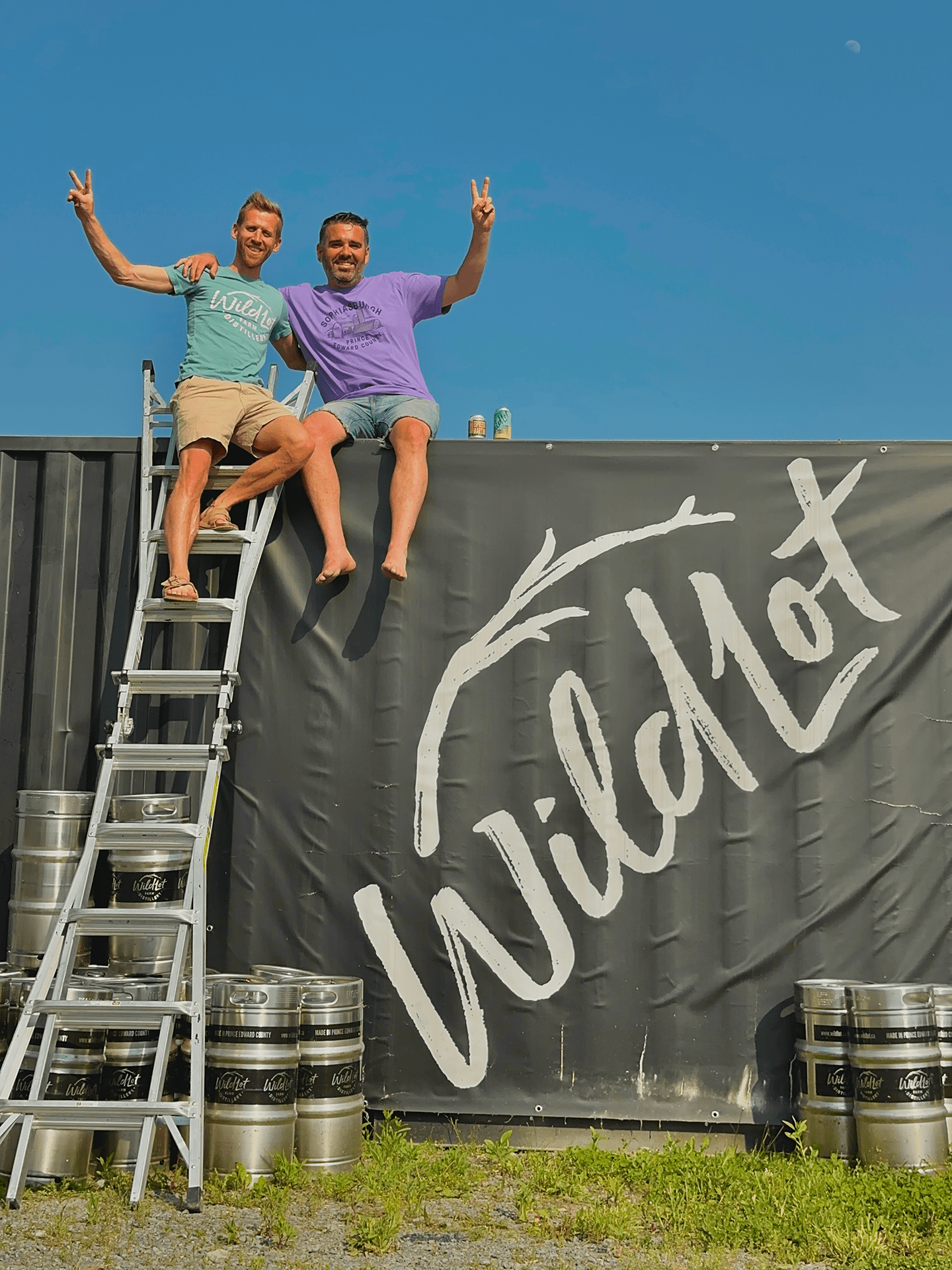 Ryan & Taylor sitting on a container with 'Wildiot' branding, surrounded by barrels.