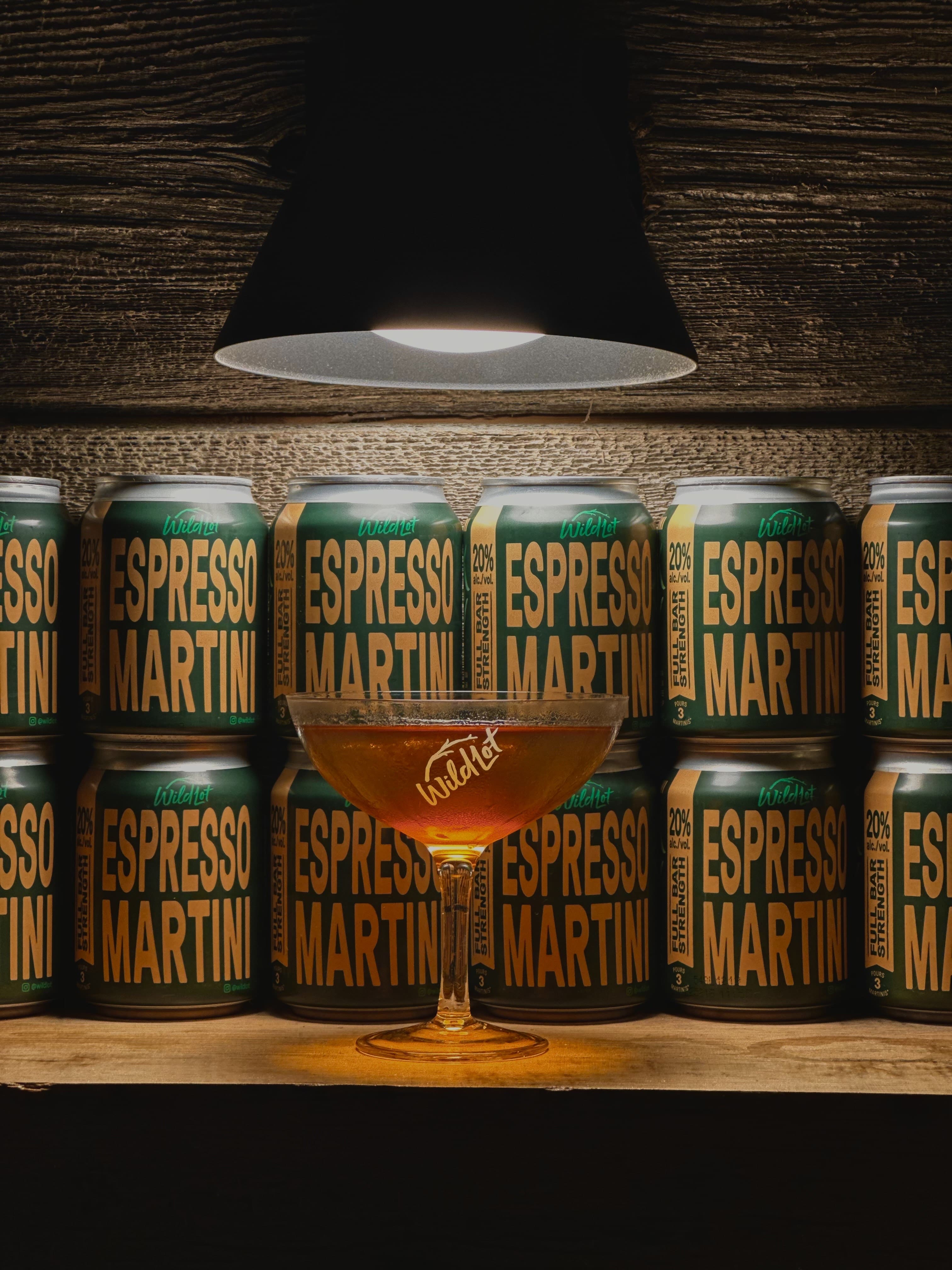 Espresso Martini cans with a cocktail glass on a wooden surface